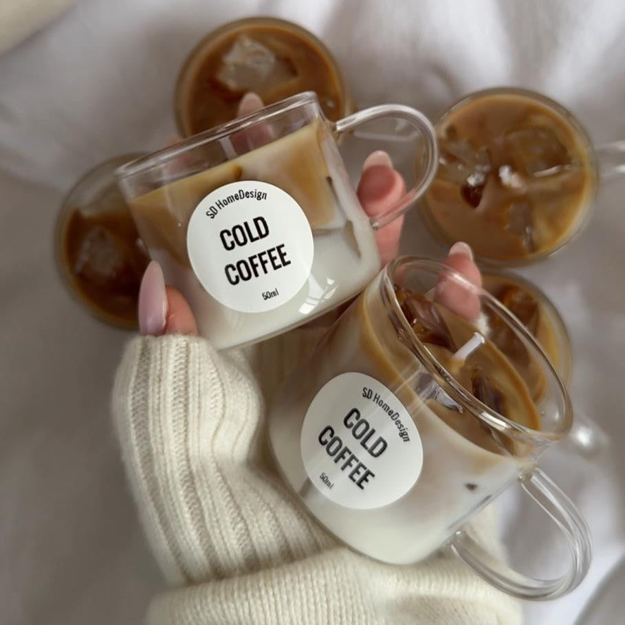 Two clear mugs with 'Cold Coffee' labels held by a person wearing a white sweater.